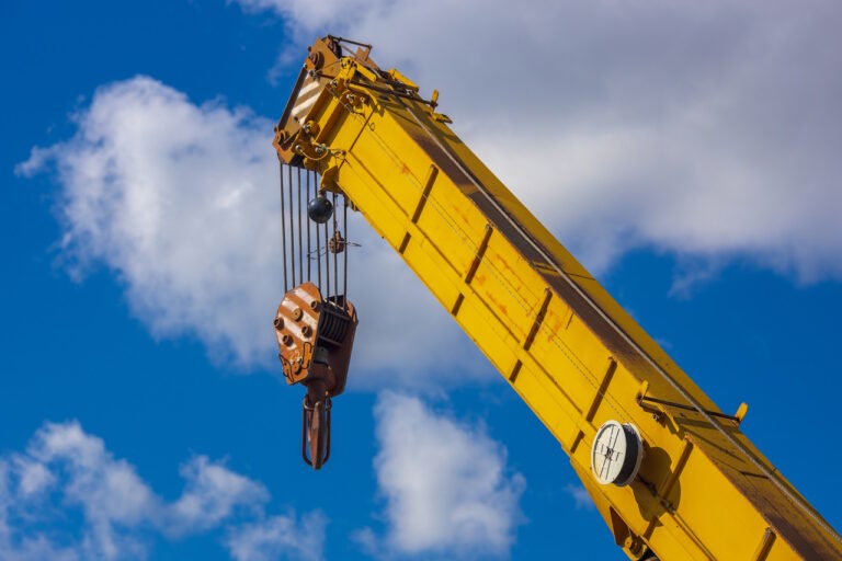 Yellow boom of a loading crane against a blue sky with clouds.